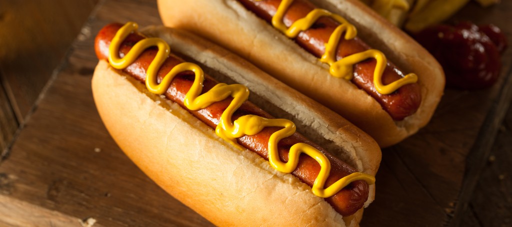 Two grilled hot dogs in toasted buns, topped with bright yellow mustard, arranged on a rustic wooden table for a warm, appetizing meal.
