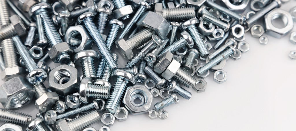 Close-up of shiny metal screws, bolts, nuts, washers, and threaded hardware scattered on a white surface, creating an industrial texture.