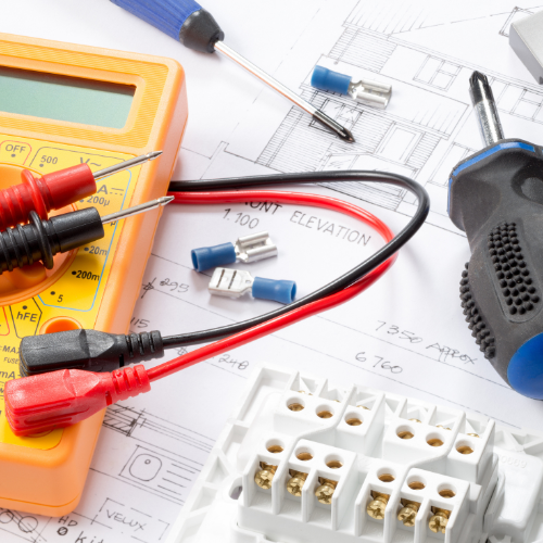 Electrical tools and components on architectural plans, featuring a multimeter, screwdrivers, and connectors, conveying a sense of technical work.