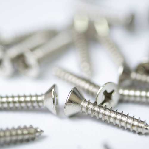 Close-up of several shiny silver screws with flat, slotted heads scattered on a white surface. The image conveys a sense of organization and utility.