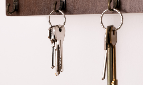 A wooden key rack with two sets of keys hanging on metal hooks against a white wall. The image gives a sense of organization and simplicity.