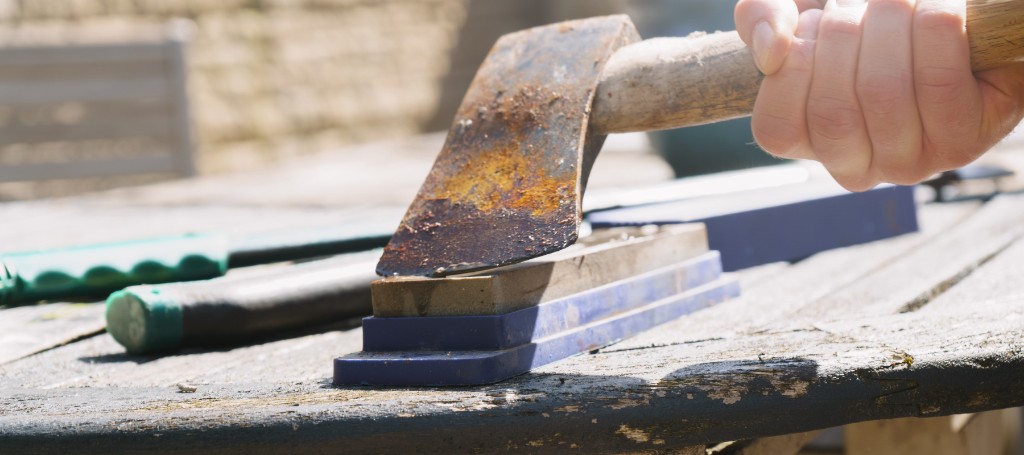 Close-up of a hand wielding a rusty hammer over a small anvil on a workbench, evoking hands-on metalworking and craftsmanship.