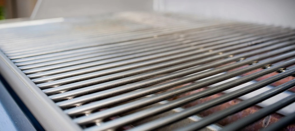 A white propane tank with a brass valve sits in front of an open black barbecue grill, suggesting a ready-to-use outdoor cookout.