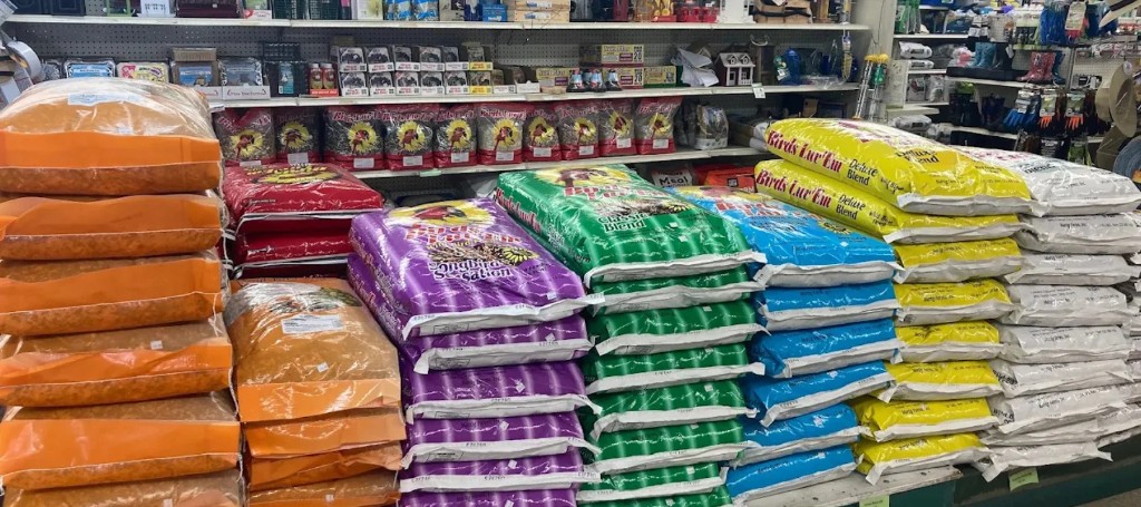 A grocery store aisle displays tall stacks of colorful rice and grain bags in orange, purple, green, blue, yellow, and white, creating a busy, well-stocked feel.