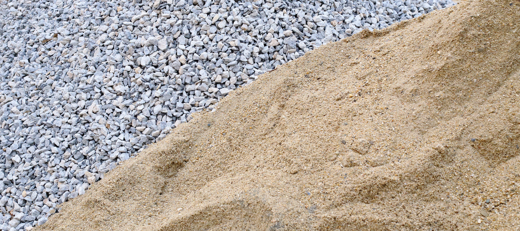 Close-up of pale tan sand beside gray gravel, forming a textured diagonal boundary; a neutral, earthy construction-material scene.