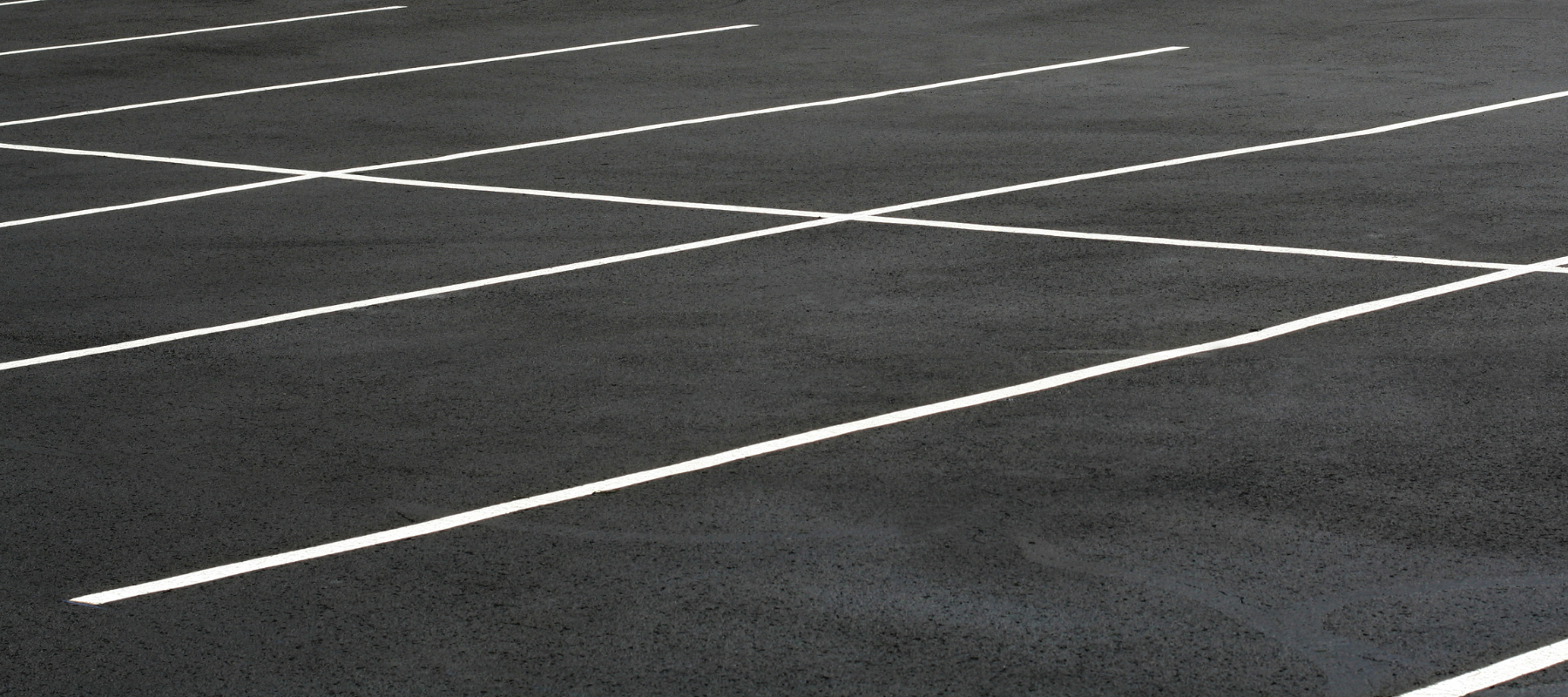 Empty asphalt parking lot marked with crisp white lines forming geometric patterns, creating a stark, orderly, minimalist, and quiet atmosphere.