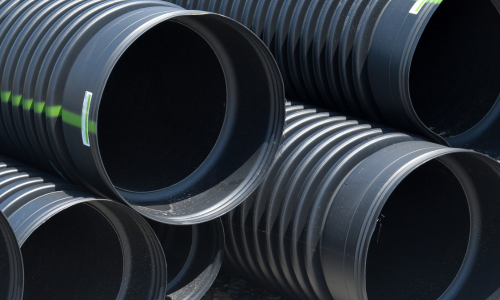 Close-up of tightly coiled black hoses or tubing, layered in curved bands with scattered dust, grass, and debris, creating an industrial texture.