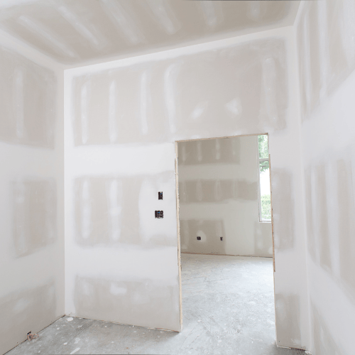 A quiet, empty white room with built-in shelves and an open doorway leading to a brighter adjoining space; soft, muted light creates a minimalist mood.