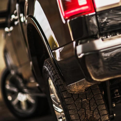 Close-up of a polished black SUV's rear wheel, rugged tire, and glowing red taillight in dramatic low light, conveying a rugged, premium feel.