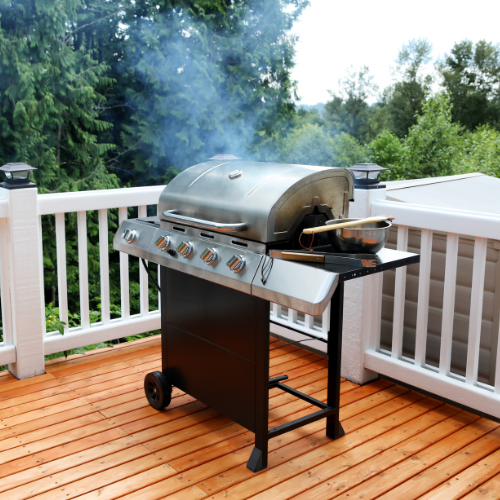 A silver grill on a wooden deck steaming with a pan on the side, surrounded by lush green trees