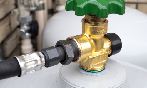 Close-up of a brass gas valve with a green turn handle, connected by a black hose. The setting is industrial, conveying functionality and precision.
