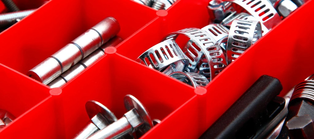 Close-up of red organizer bins filled with shiny metal tools and hardware, including sockets, clamps, rods, and a black-handled tool.