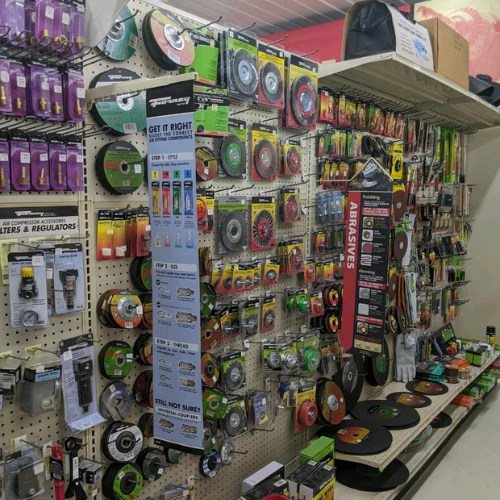 Hardware store aisle displaying pegboards packed with saw blades, drill accessories, filters, regulators, tools, and automotive supplies.