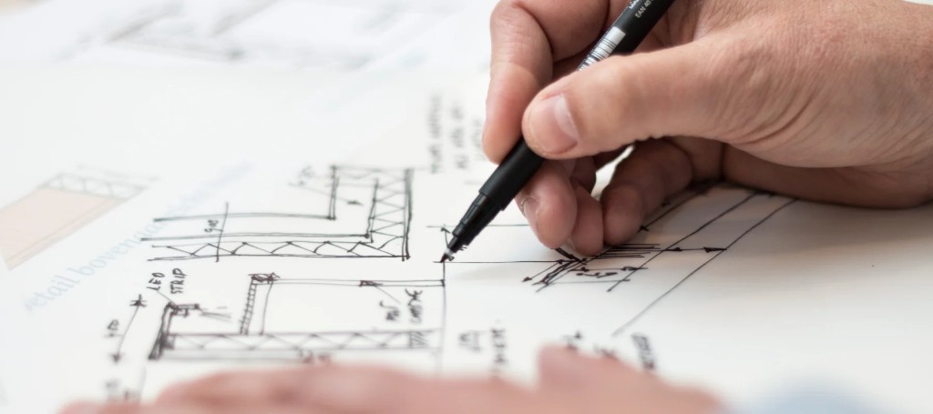 Close-up of an architect's hand using a black pen to draw detailed building blueprints on white paper, conveying precision and focus.