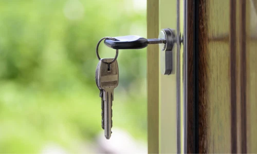 Close-up of a metal key in a door lock, with a blurred green outdoor background, symbolizing access, security, and new opportunity.