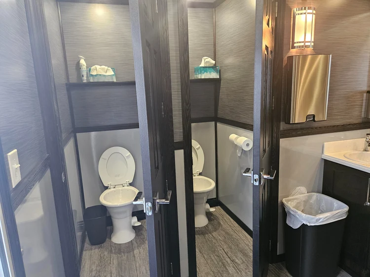 A compact modern bathroom with dark cabinets, a wood floor, two framed prints, and a wide mirror above the sink; its neutral palette feels calm and tidy.