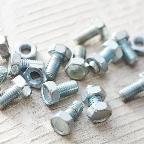 A scattered assortment of silver hex-head bolts, threaded screws, and nuts lies on a pale, weathered wooden surface, creating a practical workshop tone.