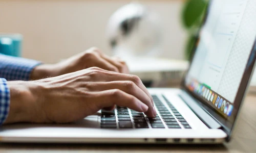 Close-up of hands typing on a laptop keyboard at a desk, with a document open on screen.